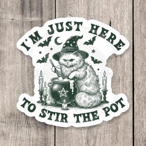 May include: A sticker featuring a fluffy cat wearing a witch hat, stirring a cauldron. The text reads "I'M JUST HERE TO STIR THE POT". Bats, stars, and candles surround the cat and cauldron, creating a Halloween theme.