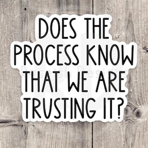 May include: A white sticker with black text on a wooden background. The sticker reads, "DOES THE PROCESS KNOW THAT WE ARE TRUSTING IT?" in a bold, sans-serif font. The background is a light brown, rustic wood.