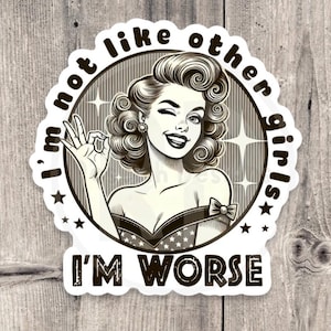 May include: A black and white sticker featuring a retro illustration of a woman winking and making an "okay" hand gesture. The text reads "I'm not like other girls, I'm worse" in a circular and rectangular layout.