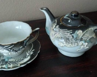 Può includere: Una tazza da tè e un piattino bianchi con un motivo di drago bianco e nero. Una teiera abbinata con un motivo di drago bianco e nero.