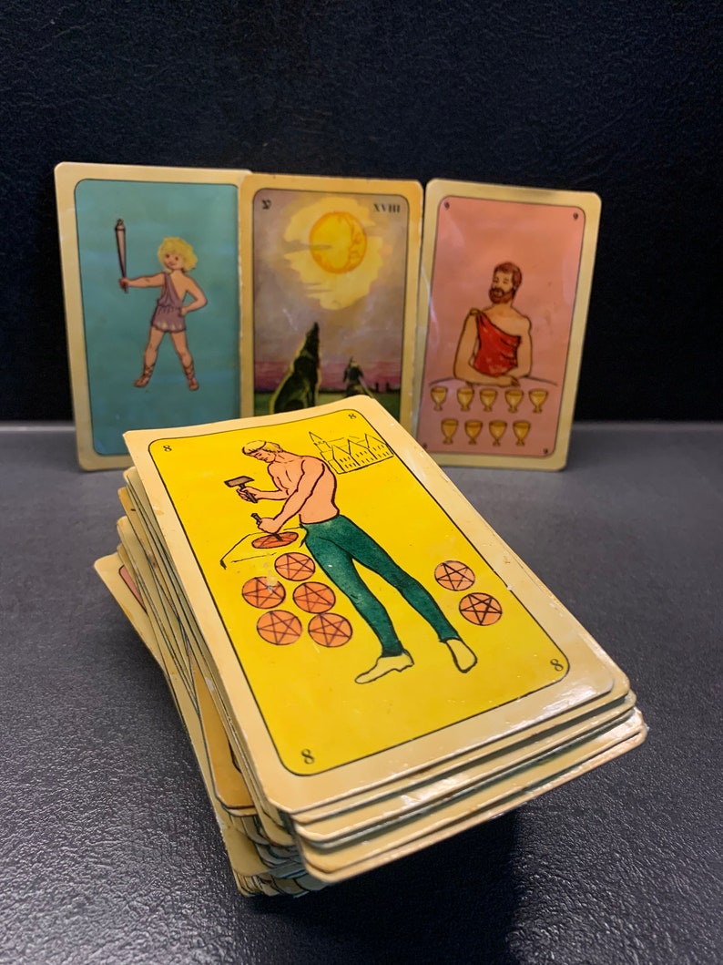 Puede incluir: Una baraja de cartas de tarot con ilustraciones coloridas. Las cartas est&aacute;n apiladas una encima de la otra y muestran una variedad de im&aacute;genes, incluyendo un hombre con un martillo, un lobo y un hombre con una copa. Las cartas son amarillas con n&uacute;meros negros en las esquinas.