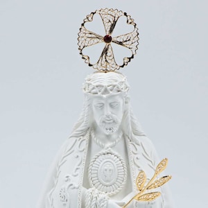 Peut inclure: Statue en céramique blanche de Jésus-Christ avec une couronne d'épines dorée, une auréole dorée et une branche d'olivier dorée. La statue est sur un piédestal blanc avec l'inscription "SENHOR SANTO CRISTO".