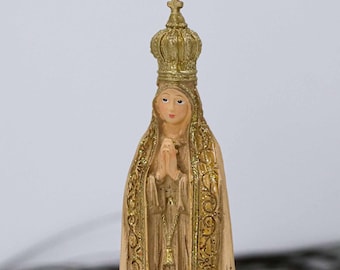 Puede incluir: Una figurita de la Virgen María, con una corona dorada y una túnica blanca con ribetes dorados. Ella tiene sus manos en oración.