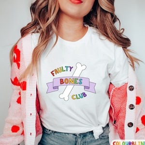 May include: White t-shirt with a rainbow graphic of a bone with the text "Faulty Bones Club".