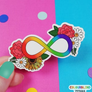 May include: A rainbow infinity symbol with flowers and a sunflower surrounding it. The infinity symbol is white with a rainbow gradient. The flowers are red, white, and yellow.