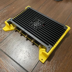 May include: A black electronic device with a yellow plastic housing and a cooling fan. The device has four antenna ports labeled "GPS", "PRS", "PRS", and "L1/S".