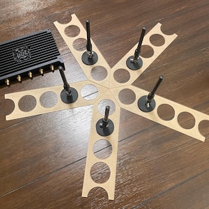 May include: A black device with multiple antennas and a heat sink, surrounded by six brown cardboard circles with cutouts for the antennas. The device is on a wooden surface.