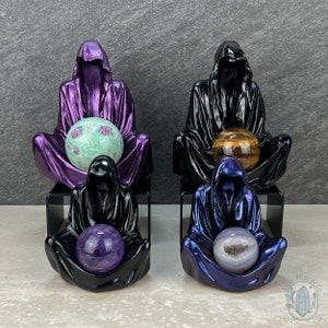 May include: Four black hooded figures, each holding a different coloured orb. The orbs are green, brown, purple, and white. The figures are sitting on black stands.