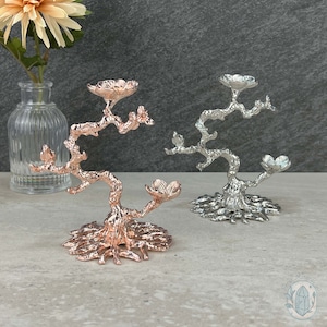 May include: Two decorative tree-shaped ring holders, one in silver and one in rose gold. The holders are made of metal and have a detailed, textured finish.