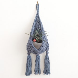 May include: A blue crocheted hanging planter with tassels, holding a small potted plant.