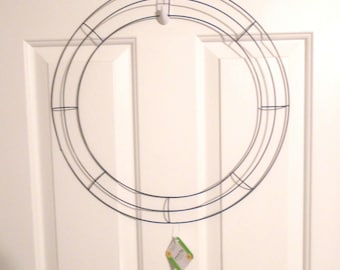 May include: A silver metal wreath frame with a blue wire design. The frame is hanging on a white door.