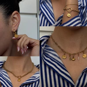 May include: A set of gold-toned jewelry featuring a necklace with a charm, a pair of earrings with charms, and a bracelet with a charm. The charms are all different shapes and sizes, and they are all made of gold-toned metal.