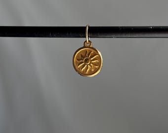 May include: Gold charm with a sun design. The charm is round and has a raised sun design with rays emanating from the center.