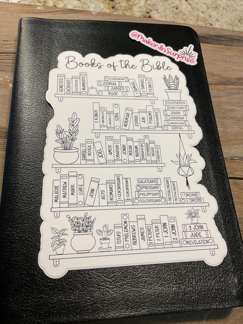 May include: A black Bible with a white sticker featuring a bookshelf design. The sticker lists the books of the Bible in a decorative font, with small potted plants. The sticker has the text "Books of the Bible".