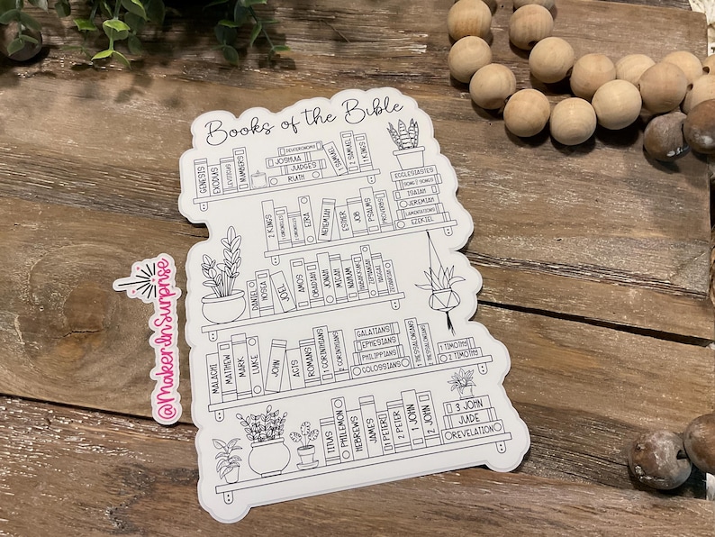 May include: A white sticker with a bookshelf design, featuring the words "Books of the Bible" at the top. The sticker includes the names of the books of the Bible, arranged as if they were on shelves, with potted plants. A small sticker with the text "@MakerInSurprise" is also present.