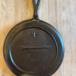 May include: A cast iron skillet with a black finish and a loop handle. The skillet has the number "7" embossed on the surface.