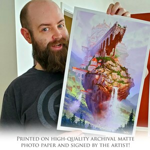 Może przedstawiać: Osoba trzyma wydruk ilustracji fantasy. Ilustracja przedstawia duże, unoszące się miasto zbudowane na skalistej skarpie z wodospadami spływającymi po bokach. Miasto jest zbudowane z białego kamienia i ma wiele wież i wieżyczek. Niebo jest jasnoniebieskie z puszystymi chmurami. Wydruk jest drukowany na wysokiej jakości matowym papierze fotograficznym archiwalnym i podpisany przez artystę.