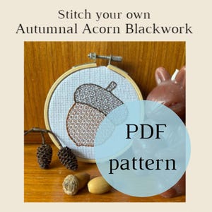 May include: A brown and white acorn cross stitch pattern in a wooden embroidery hoop. The hoop is on a wooden surface with a brown candle and pine cones. The text "PDF pattern" is on a blue circle.