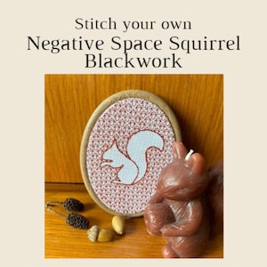 Puede incluir: Un diseño de punto de cruz de una ardilla blanca en un marco ovalado de madera. El diseño está hecho con hilo rojo y blanco y presenta una ardilla con una cola tupida. El marco está sobre una superficie de madera con una pequeña figura de ardilla y bellotas.