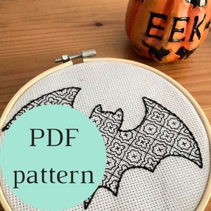 Può includere: Un motivo a punto croce in bianco e nero a forma di pipistrello in un telaio da ricamo in legno. Il design del pipistrello presenta un motivo geometrico dettagliato. Le parole "PDF pattern" sono in un cerchio turchese. Una piccola zucca con la parola "EEK".