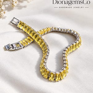 Op de afbeelding: Een zilverkleurige armband met een doorlopende rij rechthoekige, baguette-geslepen gele edelstenen. Het sieraad is voorzien van een veilige metalen baksluiting. De tekst DionagemsCo HANDMADE JEWELRY is zichtbaar in de rechterbovenhoek van de afbeelding.