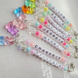 May include: A set of eight colorful gummy bear charm bracelets with the names of the members of the K-pop group Stray Kids spelled out in white beads. The names are: Jisung, Felix, Seungmin, Lee Know, Jeongin, Hyunjin, Changbin, and Bang Chan.