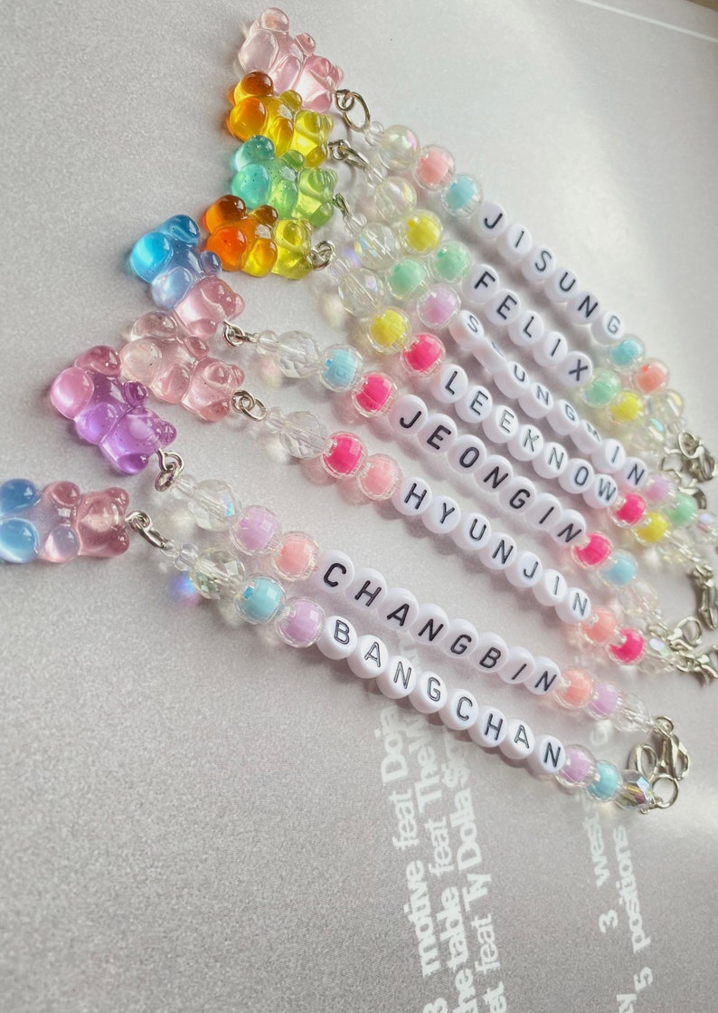May include: A set of eight colorful gummy bear charm bracelets with the names of the members of the K-pop group Stray Kids spelled out in white beads. The names are: Jisung, Felix, Seungmin, Lee Know, Jeongin, Hyunjin, Changbin, and Bang Chan.