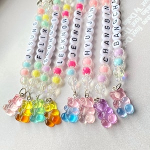 May include: Eight colorful beaded keychains with gummy bear charms. Each keychain features a different name: Jisung, Felix, Seungmin, Leeknow, Jeongin, Hyunjin, Changbin, and Bangchan.