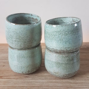 May include: Four ceramic mugs in a light green color with a speckled glaze. The mugs are stacked in pairs.