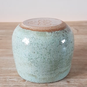 May include: A light green ceramic mug with a brown rim and a white design on the bottom.
