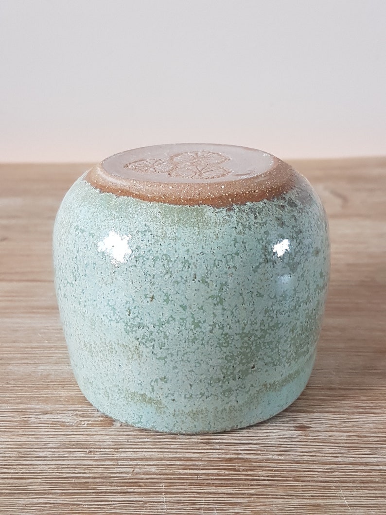 May include: A light green ceramic mug with a brown rim and a white design on the bottom.
