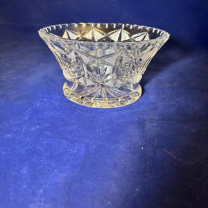 May include: A clear, cut-glass bowl with a starburst and floral pattern. The bowl has a flared rim and sits on a small, round base. The bowl is likely used for serving or display.