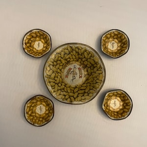 May include: A set of five vintage peanut-shaped bowls with a brown rim. The bowls are decorated with a pattern of peanuts and a cartoon peanut character. The largest bowl has the text "Planters Peanuts" on it.