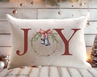 May include: Rectangular off-white pillow with the word "JOY" in burgundy letters. A watercolor wreath with a red bow and silver bells is between the "J" and "Y". The text "3 SIZE OPTIONS NATURAL OR WHITE COVERS" is at the top.