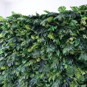 This Valar Flowers artificial tropical greenery wall features a dense, layered mix of lush foliage—including monstera leaves, palm fronds, and ferns—in rich, varied shades of green. The realistic, lifelike leaves create a fresh, jungle-inspired focal point, perfect for weddings, events, photo booths, and stylish interior decor.