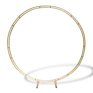 May include: Gold metal arch with a round top and three legs. The arch is made of two concentric circles.