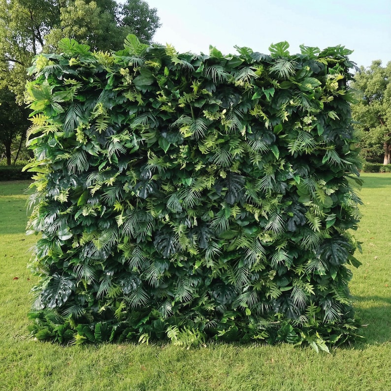 This lush, dense greenery backdrop features a mix of tropical foliage—including broad monstera leaves, delicate fern fronds, and feathery palm fronds—layered to create a vibrant, jungle-like texture. Varied shades of emerald and sage green add depth, while natural sunlight highlights the glossy, lifelike surfaces. The rich, verdant display evokes a fresh, exotic atmosphere, serving as a striking, organic focal point ideal for outdoor events or tropical-themed celebrations.