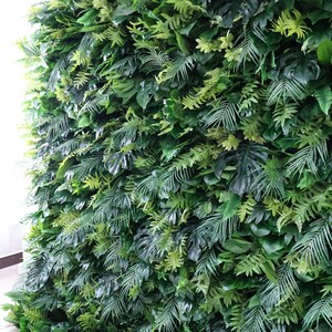 This Valar Flowers artificial tropical greenery wall is a dense, lush tapestry of lifelike foliage, featuring monstera leaves, palm fronds, and ferns in rich, varied shades of green. The layered, realistic leaves create a fresh, jungle-inspired focal point, perfect for weddings, events, photo booths, and stylish interior decor.