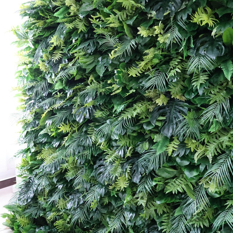 This Valar Flowers artificial tropical greenery wall is a dense, lush tapestry of lifelike foliage, featuring monstera leaves, palm fronds, and ferns in rich, varied shades of green. The layered, realistic leaves create a fresh, jungle-inspired focal point, perfect for weddings, events, photo booths, and stylish interior decor.