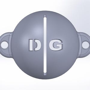 Può includere: Un oggetto sferico grigio con le lettere "IDG" ritagliate sul davanti. Una linea verticale divide la sfera. Due attacchi a forma di anello con fori sono su entrambi i lati.