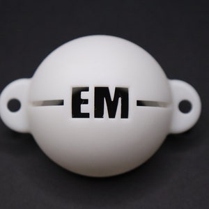Könnte beinhalten: Weißer Golfball-Retriever mit einem schwarzen "EM"-Logo.