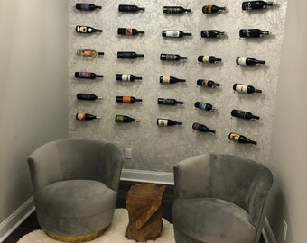 May include: A cozy corner with two gray velvet armchairs, a white fluffy rug, and a wooden side table. The wall is decorated with a wine rack featuring numerous bottles of wine.