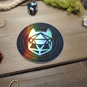May include: A holographic sticker with a black background and a white outline of a 20-sided die with a rainbow iridescent effect.