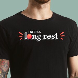 May include: A black t-shirt with the text "I need a long rest" in white with a red 20-sided die graphic.