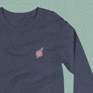 Puede incluir: Una camiseta de manga larga azul marino con un pequeño diseño bordado de un dado rojo de veinte caras con una espada que lo atraviesa.