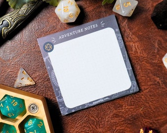 May include: A gray and white notepad with the words "Adventure Notes" printed on the top. The notepad is surrounded by dice and other gaming accessories on a brown leather surface.