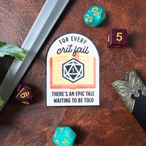 May include: A sticker with the text "For Every Crit Fail, There's an Epic Tale Waiting to be Told" and a D20 die. The image also includes a sword, and several dice in shades of teal and burgundy.