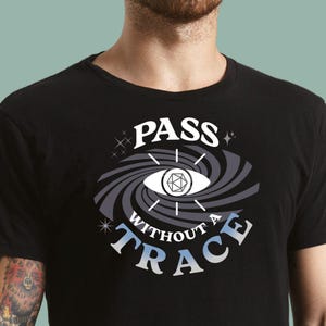 May include: Black t-shirt with a white graphic design of a swirling eye with a dice inside. The text "PASS WITHOUT A TRACE" is written around the eye.