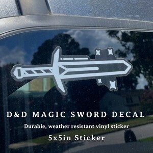 May include: A white vinyl sticker of a magic sword with stars on a car window. The sticker says "D&D Magic Sword Decal" and "Durable, weather resistant vinyl sticker" and "5x5in Sticker".
