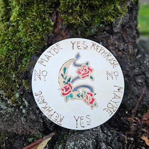May include: A wooden circle with a design of a snake and roses. The circle has the text "Yes Rephrase No: Maybe" written around the edge.